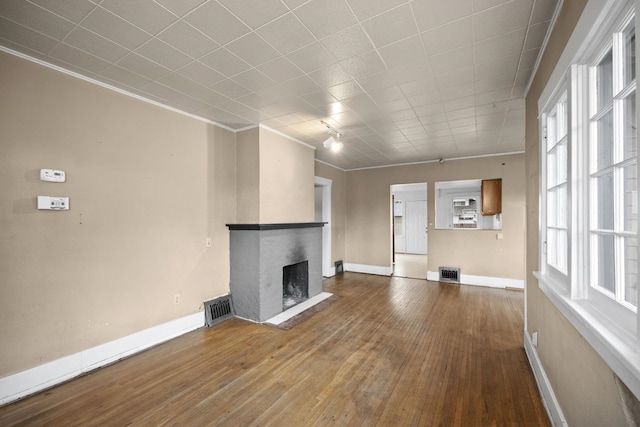 unfurnished living room with a brick fireplace, visible vents, baseboards, and wood finished floors