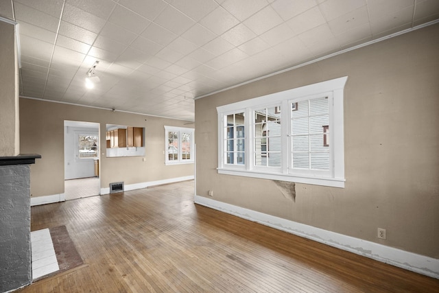 unfurnished living room with ornamental molding, wood-type flooring, visible vents, and baseboards