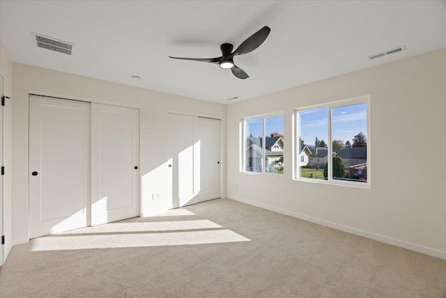 unfurnished bedroom featuring baseboards, visible vents, two closets, and light colored carpet