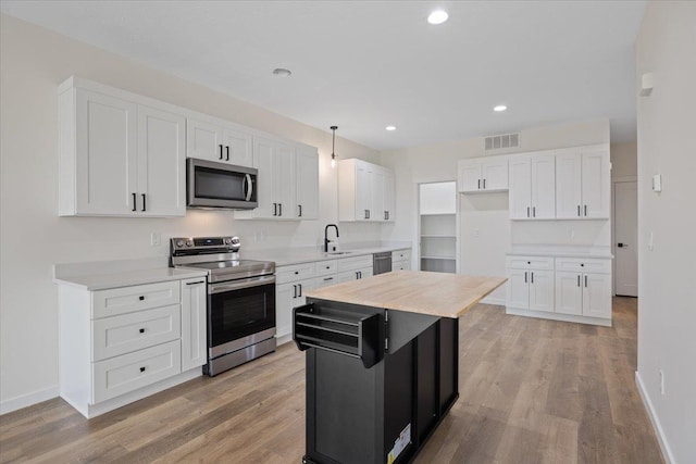 kitchen with stainless steel appliances, a sink, visible vents, light wood-style floors, and white cabinetry