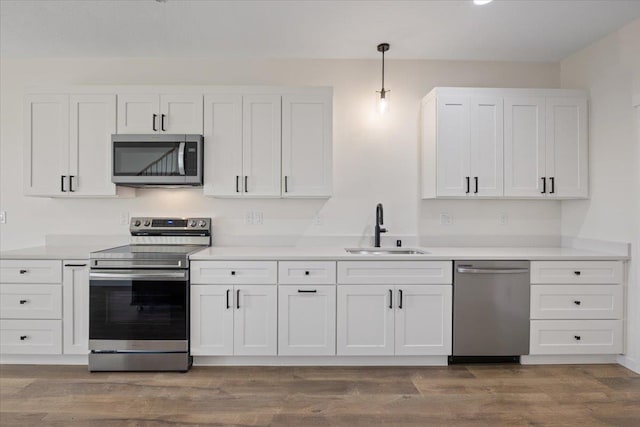 kitchen with stainless steel appliances, light countertops, white cabinetry, a sink, and wood finished floors