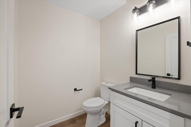 half bath featuring baseboards, vanity, toilet, and wood finished floors