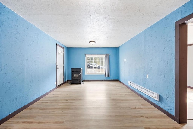 unfurnished room with a baseboard heating unit, a wood stove, and a textured wall