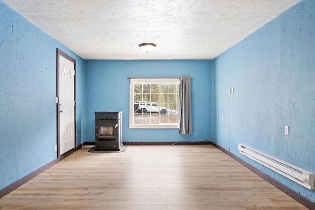 spare room with a wood stove, a baseboard heating unit, wood finished floors, and a textured wall