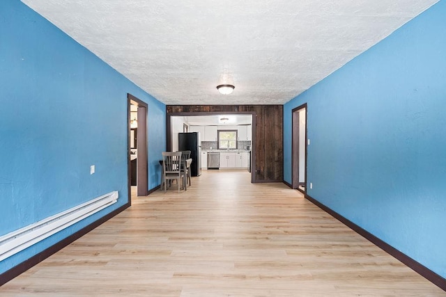 spare room featuring baseboards, a textured ceiling, light wood-type flooring, a baseboard heating unit, and a sink