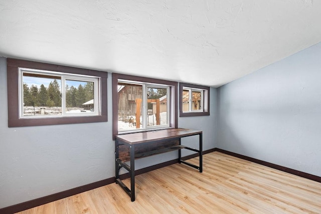 interior space featuring vaulted ceiling, light wood finished floors, a textured ceiling, and baseboards