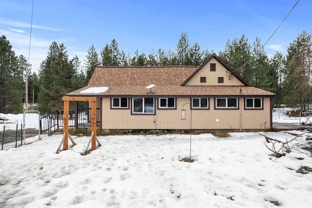 snow covered back of property featuring fence and roof with shingles