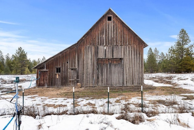 snow covered structure with an outdoor structure, a barn, and fence