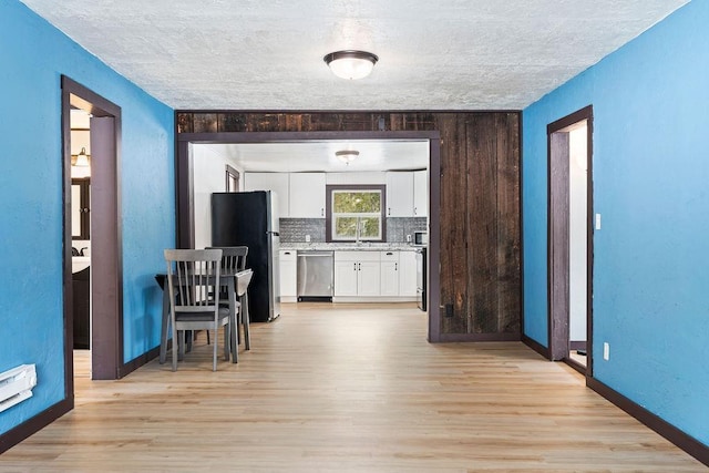 kitchen with stainless steel appliances, light countertops, backsplash, white cabinetry, and light wood-type flooring