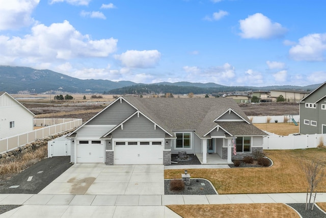 view of front facade with stone siding, concrete driveway, fence, and a mountain view