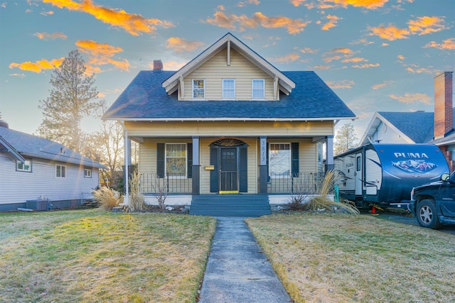 bungalow-style home with roof with shingles, a chimney, central air condition unit, a porch, and a front yard