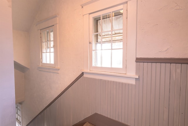 stairway with vaulted ceiling, a textured wall, and wainscoting