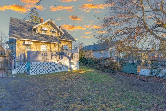 back of property at dusk with a chimney, a lawn, and a wooden deck