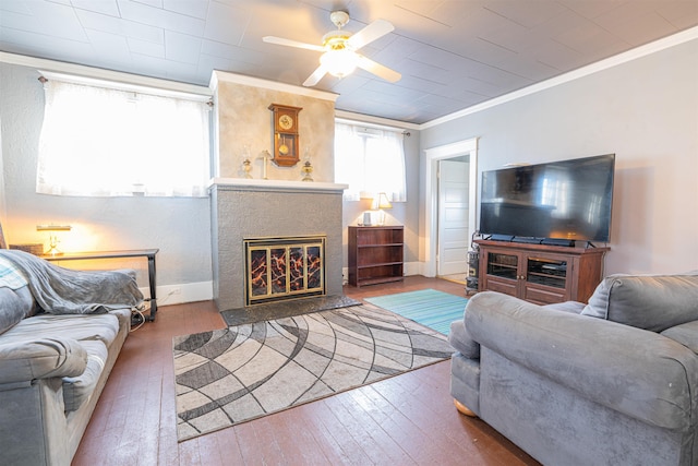 living room with ceiling fan, baseboards, hardwood / wood-style floors, a glass covered fireplace, and crown molding