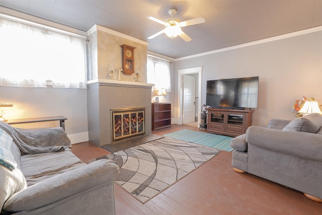 living area with baseboards, a glass covered fireplace, ceiling fan, wood finished floors, and crown molding