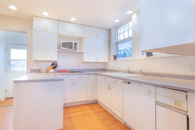 kitchen with white appliances, light wood finished floors, a sink, white cabinetry, and a wealth of natural light