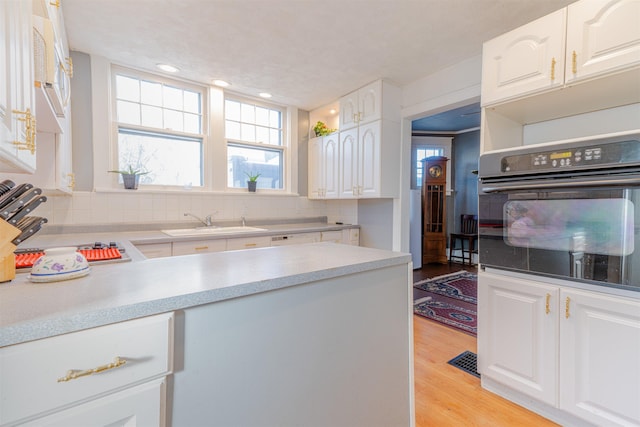 kitchen with light wood-type flooring, white cabinetry, a sink, and oven