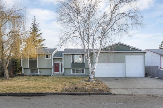 raised ranch with an attached garage, driveway, roof with shingles, and a front yard