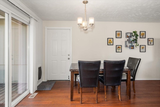 dining space featuring baseboards, visible vents, dark wood-style flooring, a textured ceiling, and a notable chandelier