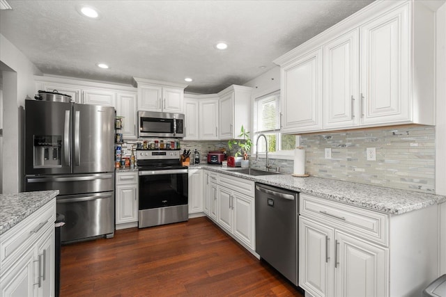 kitchen with dark wood-style flooring, light stone countertops, stainless steel appliances, white cabinetry, and a sink