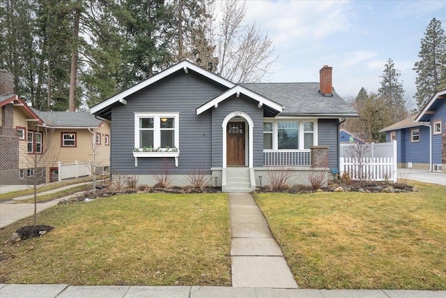 bungalow-style home featuring a shingled roof, a chimney, a front yard, and fence