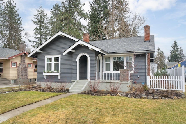 view of front of house featuring covered porch, a chimney, a front yard, and fence