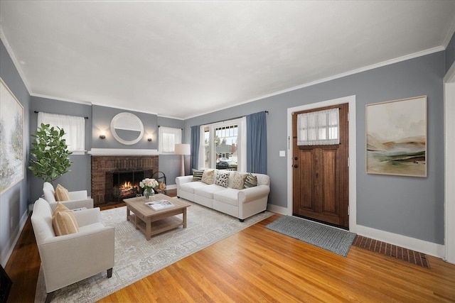 living room featuring wood finished floors, visible vents, baseboards, a brick fireplace, and crown molding