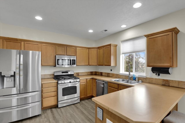 kitchen featuring visible vents, appliances with stainless steel finishes, a sink, light wood-type flooring, and a peninsula