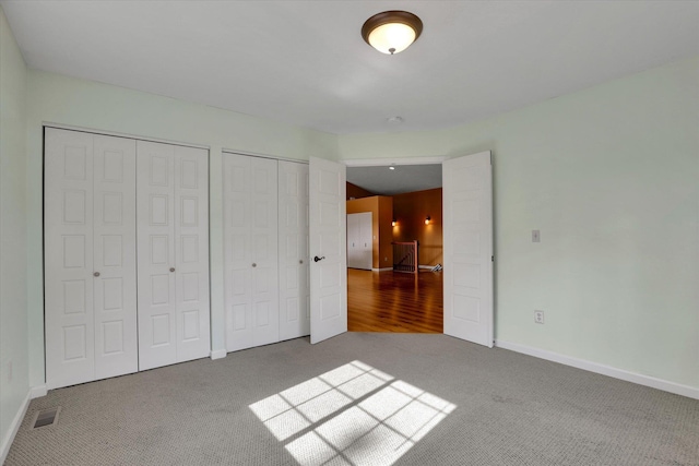 unfurnished bedroom featuring baseboards, carpet, visible vents, and multiple closets