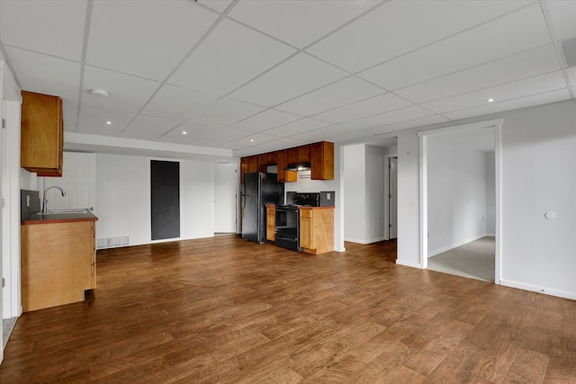 unfurnished living room with dark wood-type flooring, a paneled ceiling, a sink, and visible vents