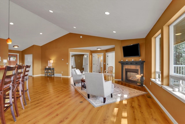 living area featuring baseboards, lofted ceiling, light wood-type flooring, a fireplace, and recessed lighting