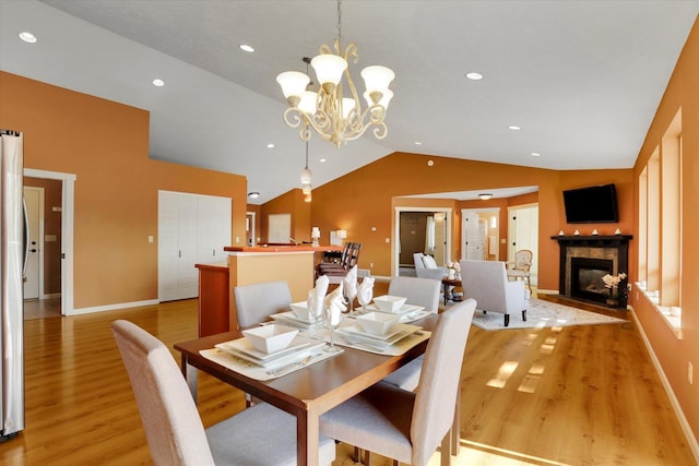 dining area with vaulted ceiling, light wood-type flooring, a fireplace with flush hearth, and baseboards