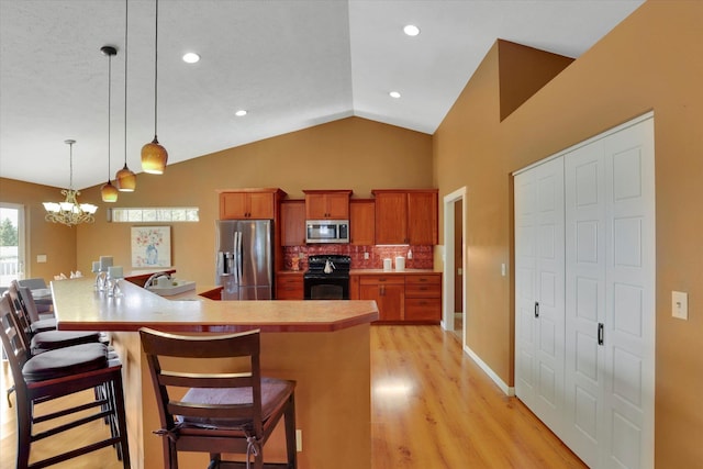 kitchen with brown cabinets, appliances with stainless steel finishes, vaulted ceiling, light wood-type flooring, and a kitchen bar