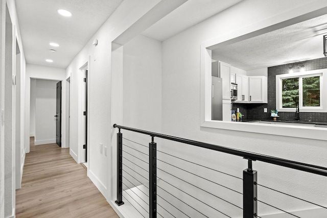 corridor with light wood finished floors, recessed lighting, a sink, an upstairs landing, and baseboards