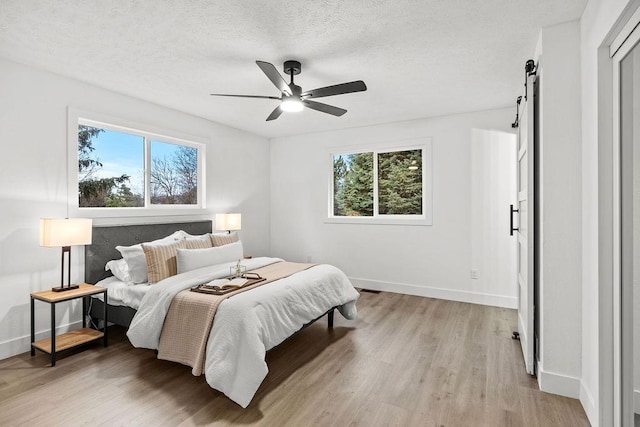 bedroom featuring a textured ceiling, ceiling fan, a barn door, baseboards, and light wood-type flooring