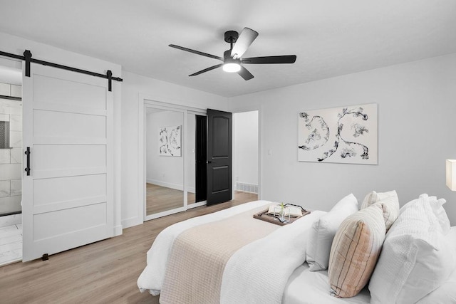 bedroom featuring light wood finished floors, a barn door, baseboards, a ceiling fan, and a closet