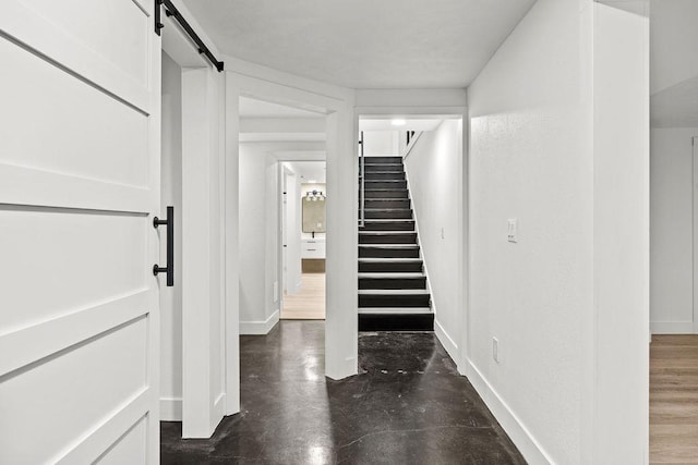 interior space featuring concrete floors, a barn door, stairs, and baseboards