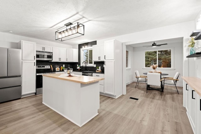 kitchen featuring tasteful backsplash, appliances with stainless steel finishes, light wood-style floors, and white cabinets