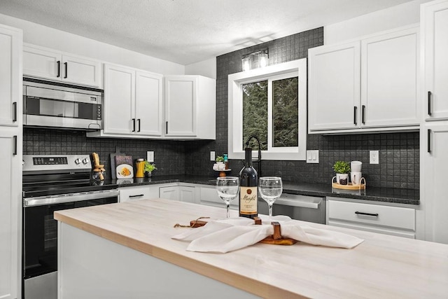 kitchen with wooden counters, backsplash, appliances with stainless steel finishes, white cabinets, and a textured ceiling