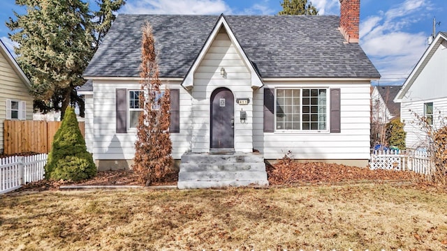 view of front of property with a shingled roof, a chimney, and fence