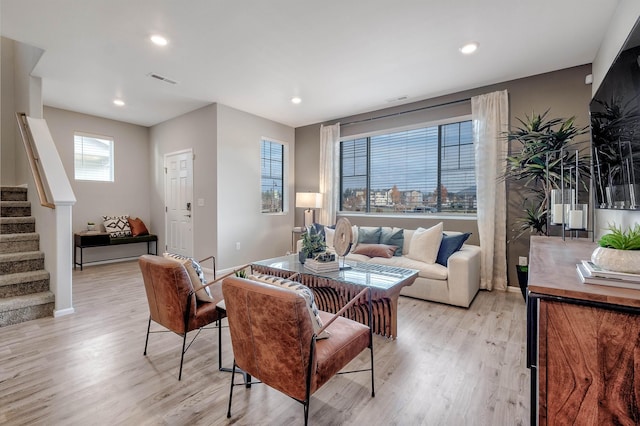 living room featuring light wood-type flooring, visible vents, stairway, and baseboards