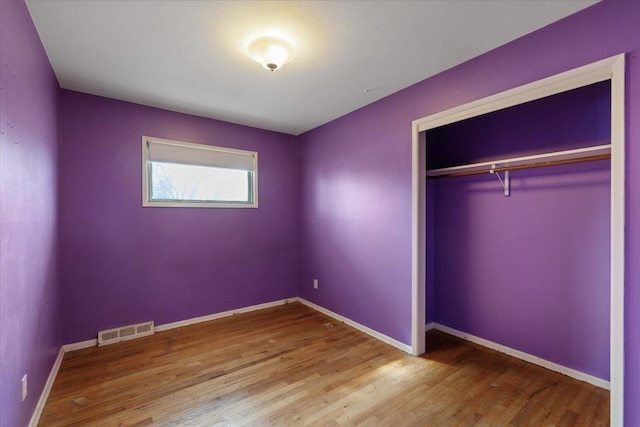 unfurnished bedroom featuring a closet, visible vents, baseboards, and wood finished floors