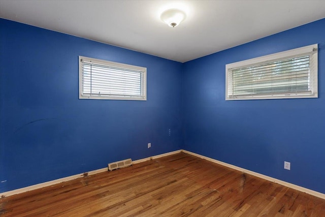 spare room featuring wood finished floors, visible vents, and baseboards