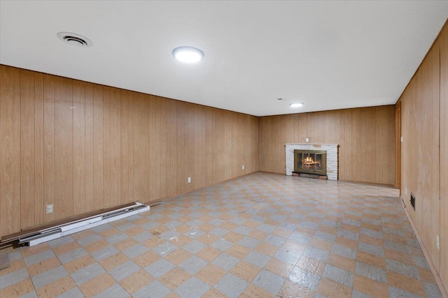 unfurnished living room with visible vents, a baseboard radiator, light floors, wood walls, and a fireplace