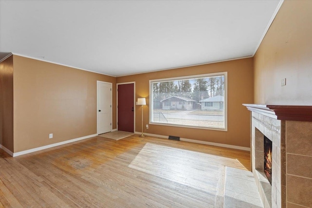 unfurnished living room with baseboards, ornamental molding, a tiled fireplace, and wood finished floors