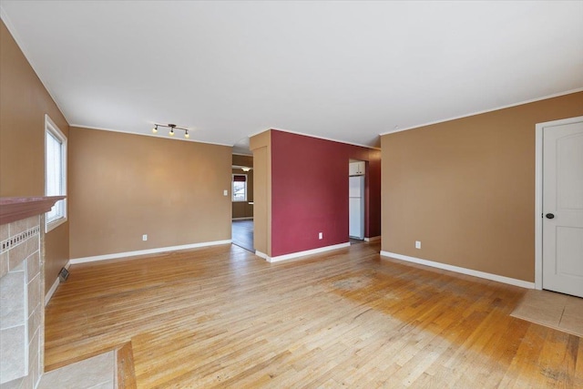 unfurnished living room with light wood-style floors, a fireplace with flush hearth, baseboards, and rail lighting