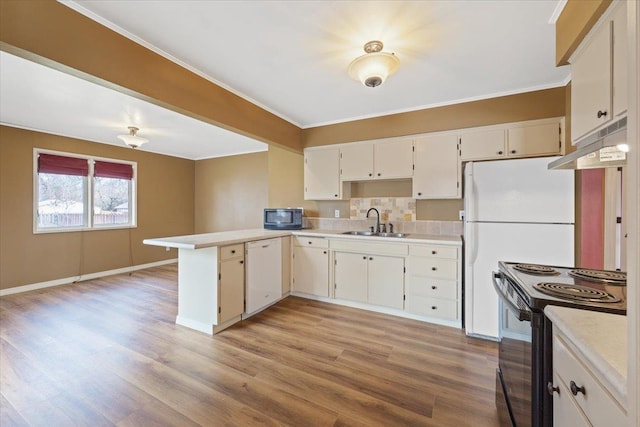 kitchen with a peninsula, under cabinet range hood, light countertops, black appliances, and a sink