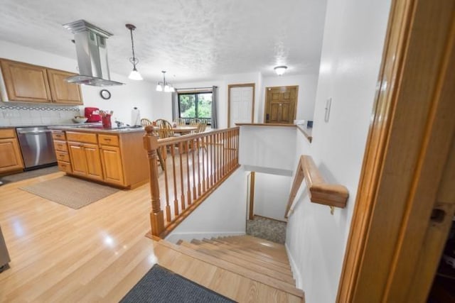 kitchen featuring wall chimney exhaust hood, stainless steel dishwasher, light wood-style floors, pendant lighting, and backsplash