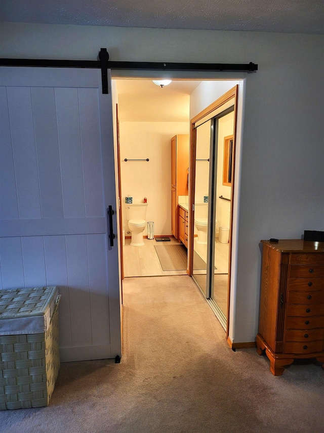 hall with a barn door and light colored carpet