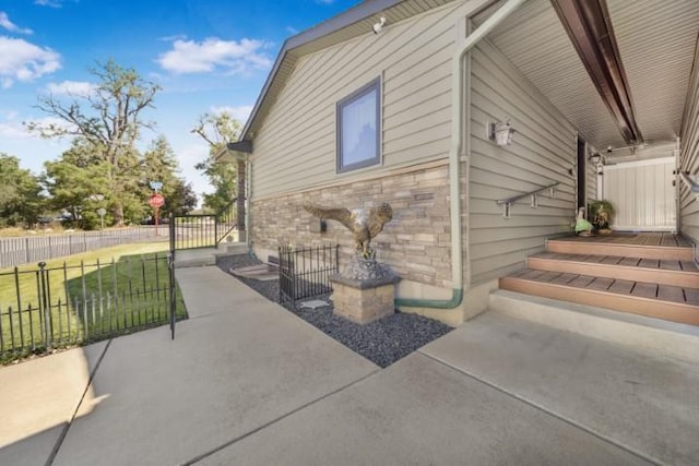 view of side of home featuring a yard, stone siding, fence, and a patio